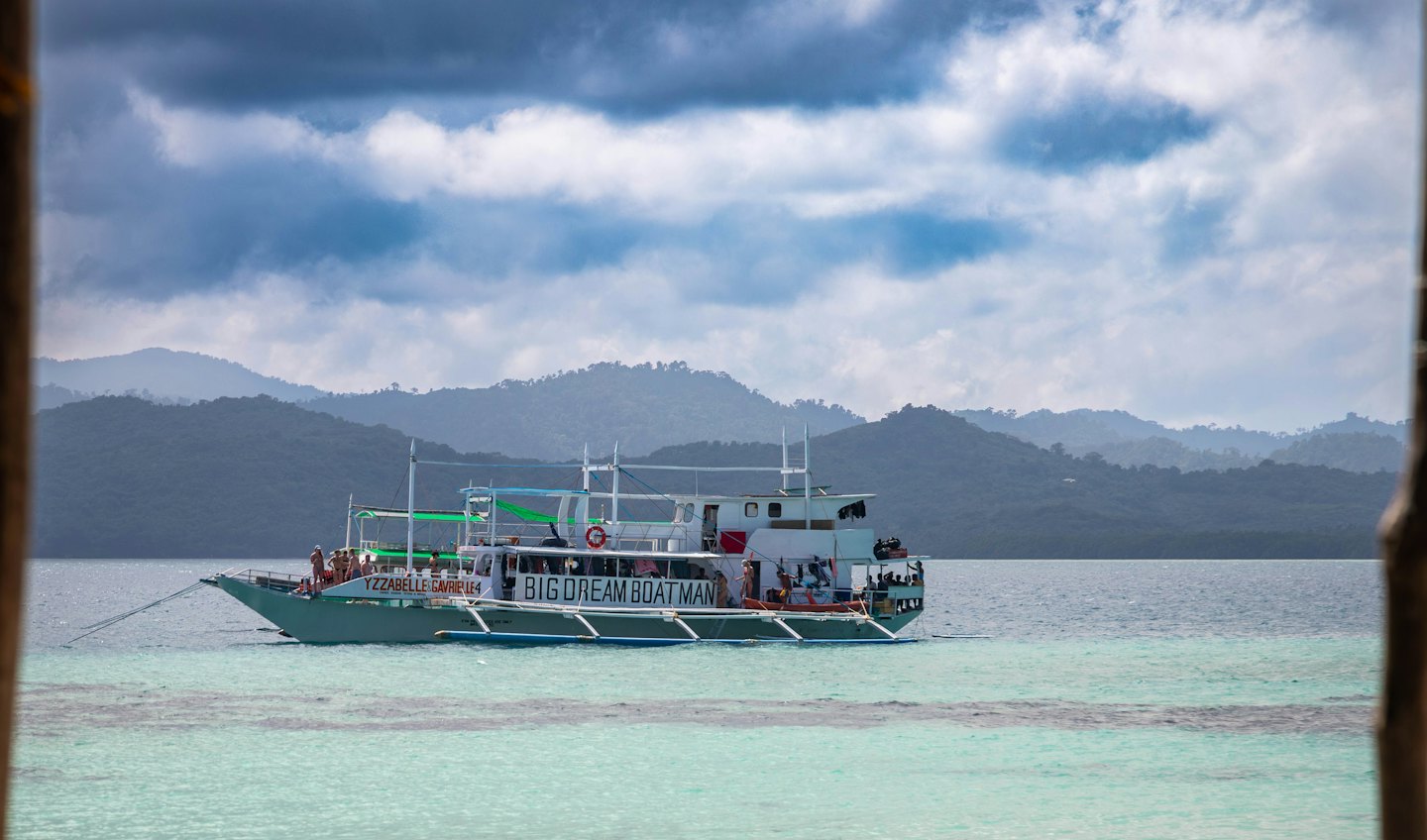 Tour boat carrying passengers across clear water toward coastal mountains.