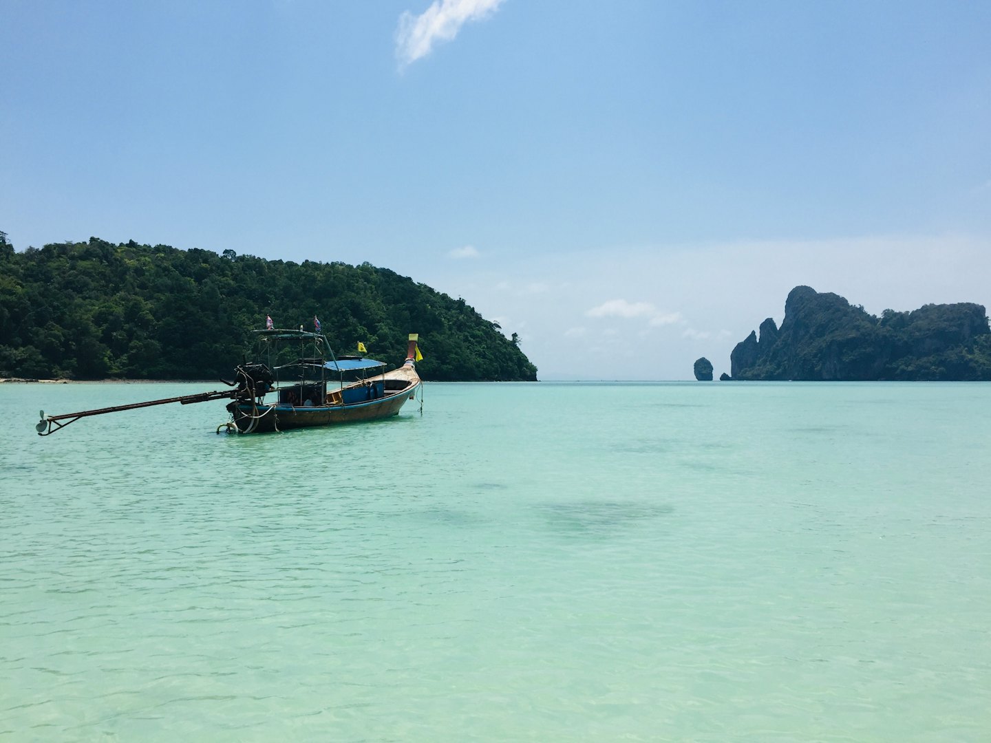 A wooden longtail boat floats in shallow tropical island waters.