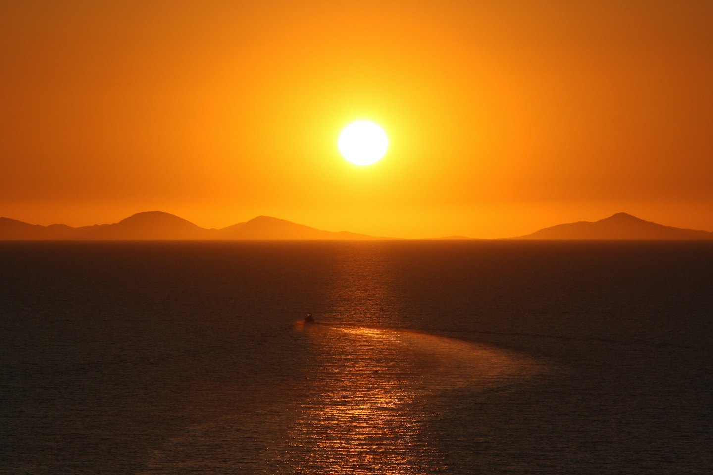 A small boat travels across the ocean during sunset.