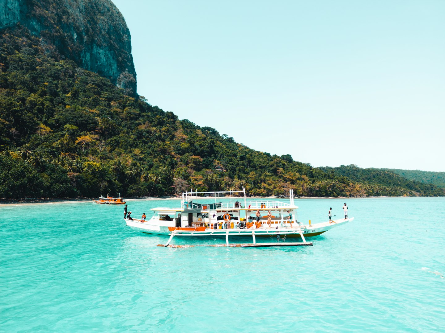 Boats travel past lush jungle cliffs on tropical waters.
