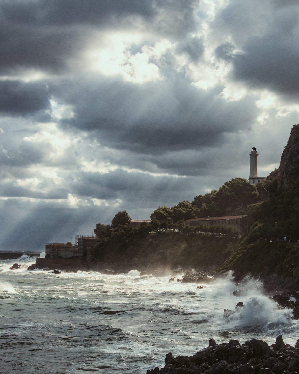 Waves crash against rocky shores below a distant white lighthouse.
