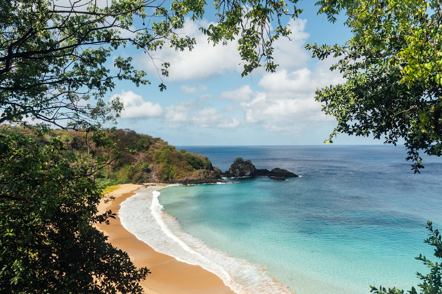 Waves roll onto a sandy beach near a rocky island.