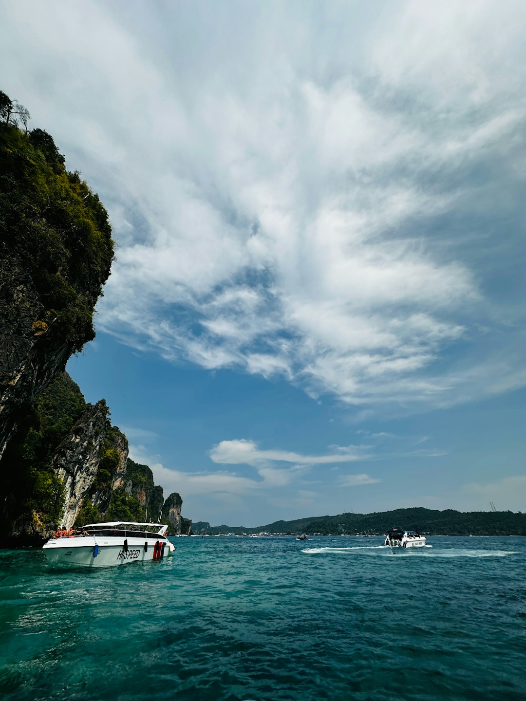 Speedboats carry tourists past towering limestone cliffs in tropical waters.